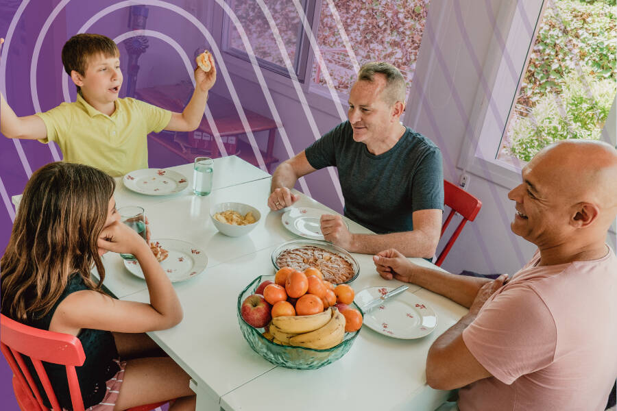 Two parents and two teenagers eating and laughing at the kitchen table